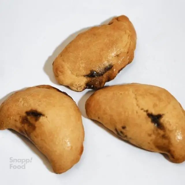 نمای نزدیک از سه شیرینی طلایی رنگ با مغز خرما یا شکلات، با سطحی نرم و پخته شده روی پس‌زمینه سفید. محصول پرو کالری (سعادت آباد).