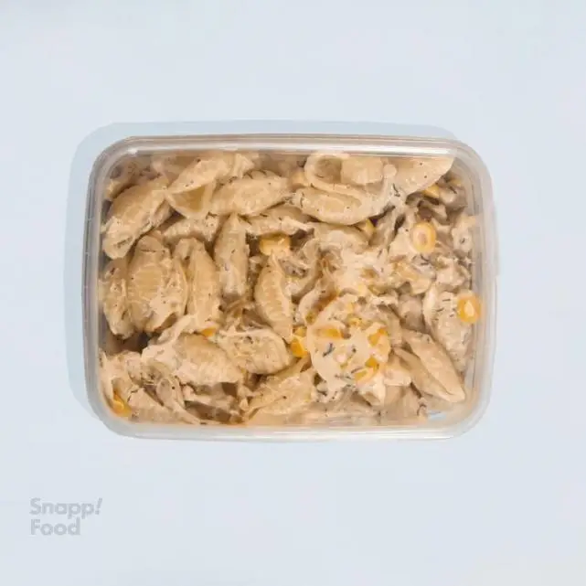 سالاد پاستا صدفی با سس خامه ای و ذرت، یک غذای رژیمی و آماده از پرو کالری سعادت آباد در ظرف شفاف پلاستیکی.