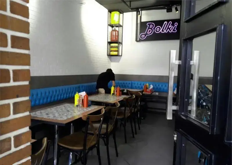 فضای داخلی تمیز و مدرن فست فود بولکی با دکوراسیون جذاب، میز و صندلی‌های چوبی و نیمکت‌های آبی رنگ برای مشتریان.
