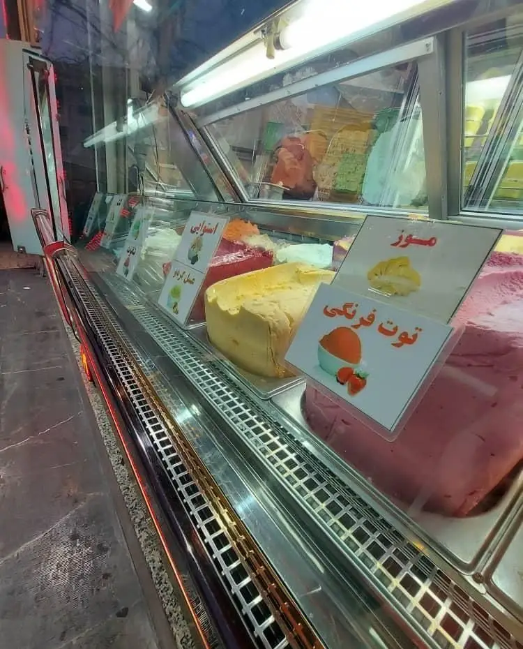 تصویری از ویترین جذاب بستنی مسعود با دسرها و بستنی‌های متنوع شامل طعم‌های موز، توت فرنگی، استوایی و عسل گردو.