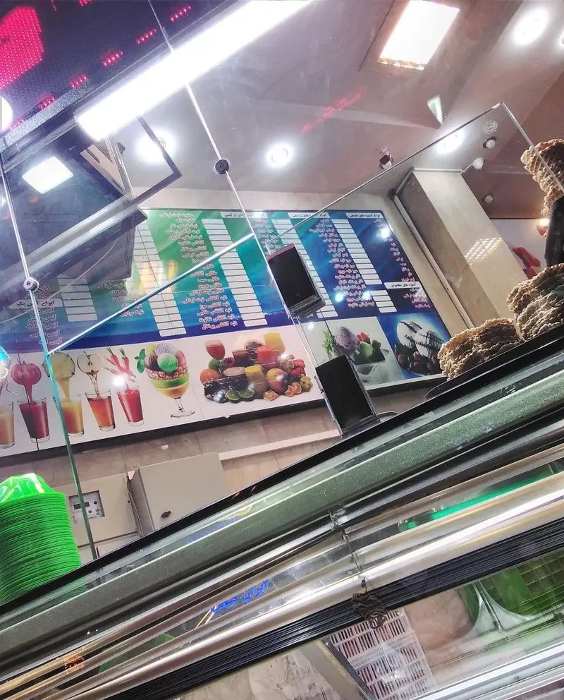 نمایی از دکوراسیون داخلی بستنی مسعود: منوی بزرگ آبمیوه‌های طبیعی و انواع بستنی، به همراه ویترین دسرهای شیرین و لیوان‌های سبز.