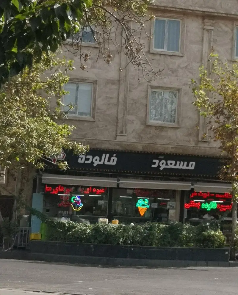 نمای بیرونی مغازه بستنی و فالوده مسعود با تابلوی بزرگ و چراغ‌های نئونی رنگارنگ بستنی قیفی در ویترین.