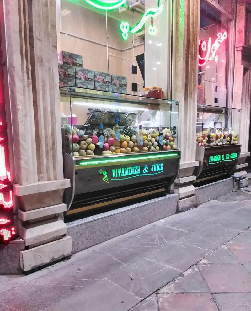 تصویری از نمای شب فروشگاه بستنی مسعود با ویترین‌های جذاب پر از میوه‌های تازه برای آبمیوه ویتامینه و بخش بستنی و فالوده.