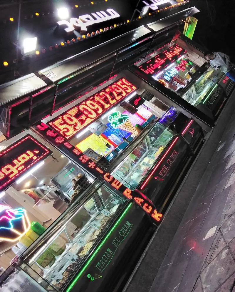 عکس شبانه از فروشگاه بستنی مسعود، با تابلوهای نئونی درخشان و ویترین‌های پر از بستنی‌های خوش‌رنگ ایتالیایی و ویژه.