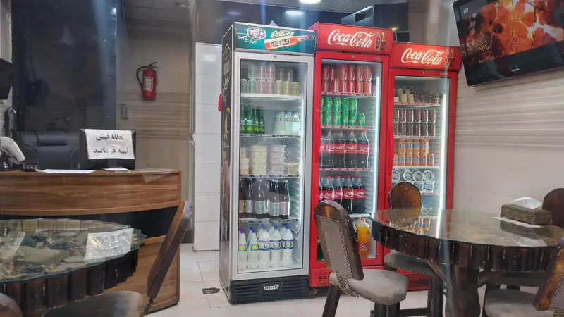 فضای داخلی فست فود آتیش با یخچال‌های بزرگ پر از نوشیدنی‌های متنوع، میز و صندلی‌های راحت و پیشخوان پذیرش مشتریان.