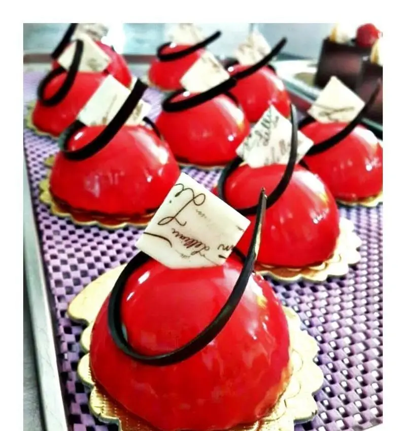 تصویری از دسرهای موس قرمز براق و لوکس شیرینی سرای پدر، با تزیینات ظریف شکلاتی، ایده‌آل برای رویدادها و لحظات شیرین