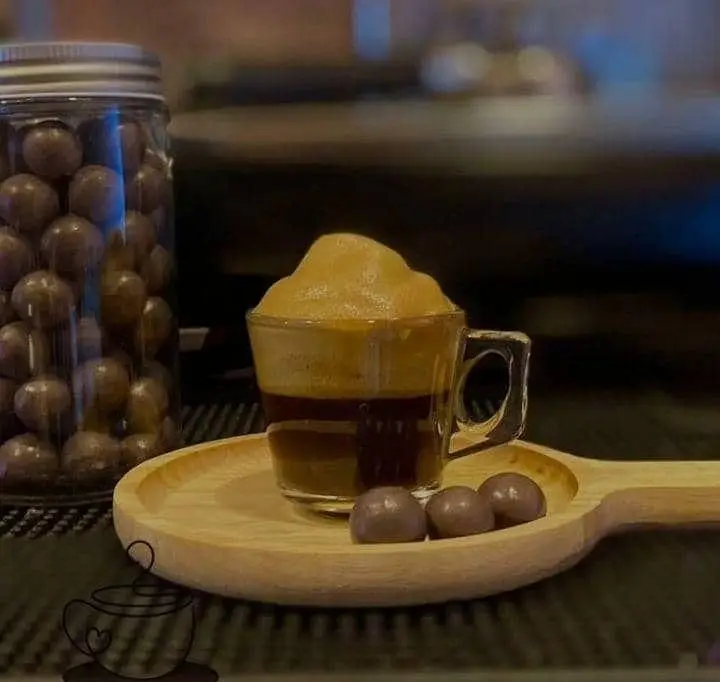 قهوه اسپرسو کافه رز با فوم غلیظ و دلپذیر، همراه با شکلات‌های توپی خوش طعم روی سینی چوبی. تجربه‌ای شیرین و به یادماندنی.