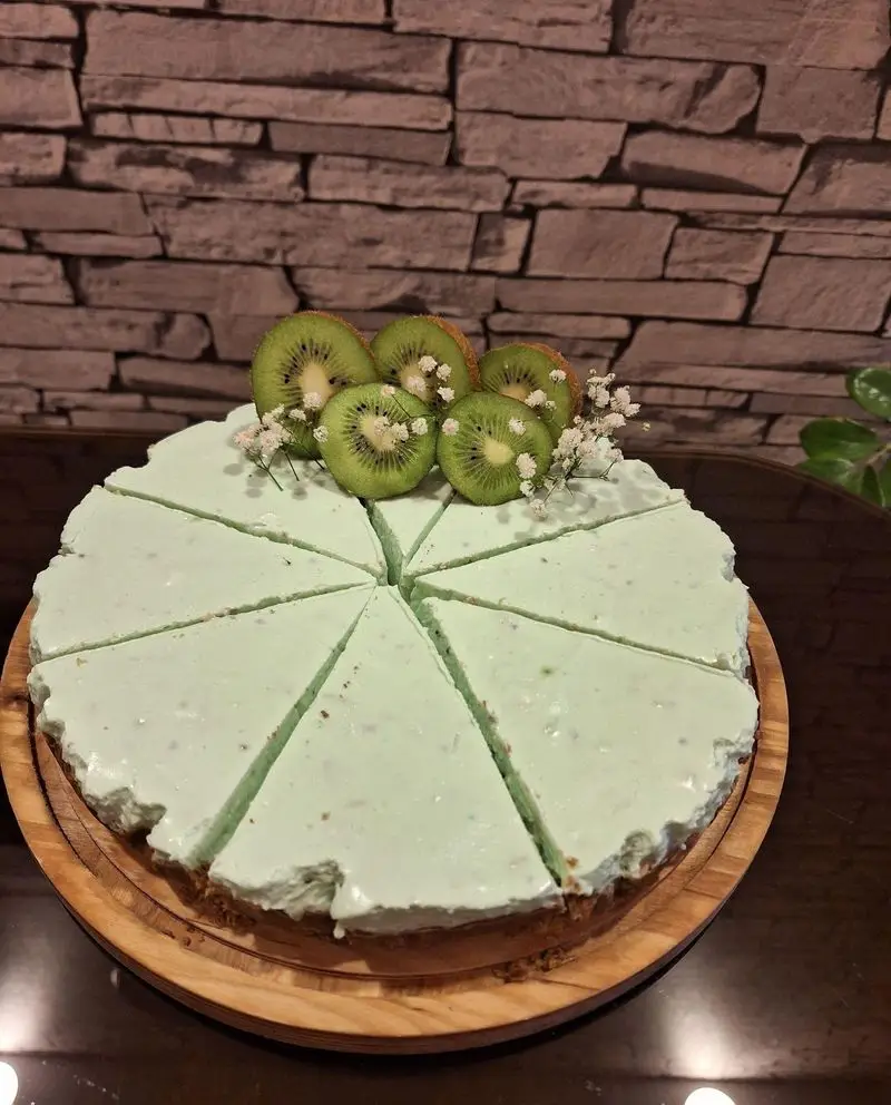 کیک چیزکیک کیوی تازه و خوشمزه کافه رز، دسر سبز رنگ با تزئین میوه و گل. بهترین انتخاب برای لحظات شیرین و دلپذیر.