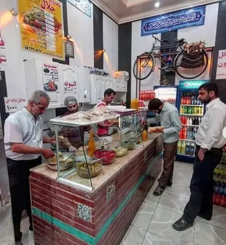 ساندویچی حلال شلوغ با آشپزهایی که مشغول آماده‌سازی انواع ساندویچ و سالاد هستند. فضای داخلی رستوران با دکوراسیون محلی.