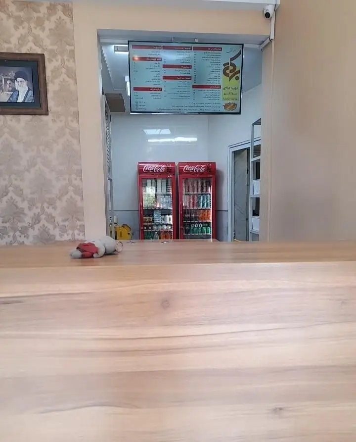 تصویری از داخل رستوران برکتی شعبه ۲: منوی غذای دیجیتال، دو یخچال نوشیدنی کوکاکولا و پیشخوان چوبی تمیز برای سفارش.
