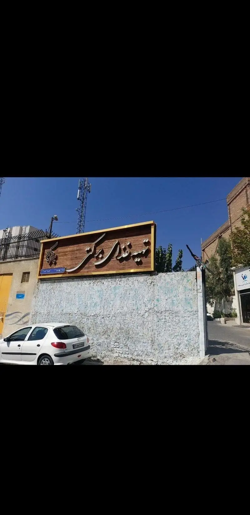 نمای بیرونی رستوران برکتی شعبه ۲ با تابلوی چوبی زیبا و طلایی، در یک روز آفتابی و ماشین سفید جلوی آن.