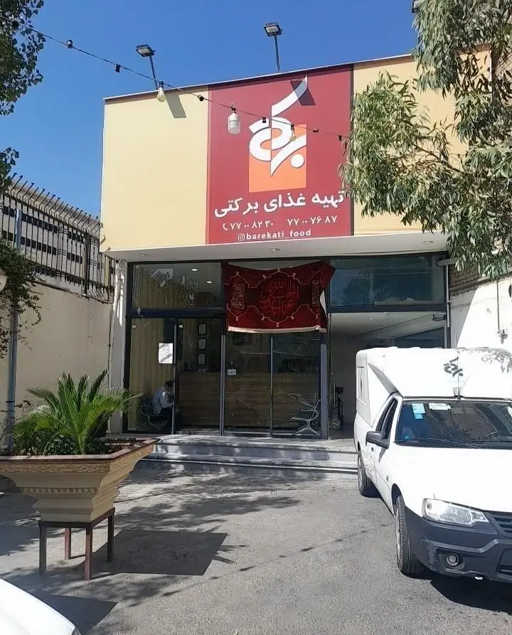 تصویر نمای بیرونی رستوران برکتی شعبه ۲، تابلوی قرمز رنگ حاوی شماره‌های ۷۷۰۰۸۲۲۰، ۷۷۰۰۷۶۸۷ و اینستاگرام @barekati_food.