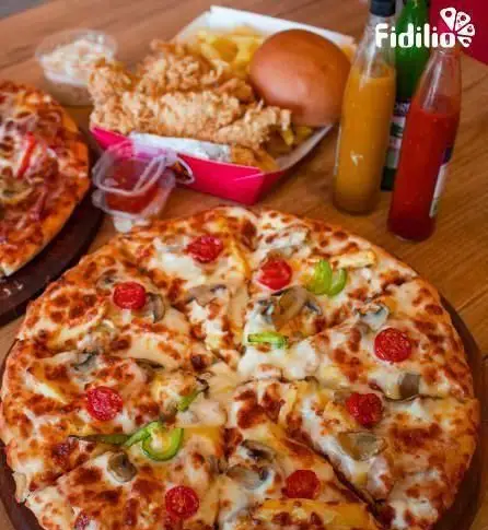 جیکی بیف: میز چوبی پر از غذاهای خوشمزه شامل دو پیتزا، مرغ سوخاری با سیب زمینی و نان، و سس‌های مختلف. بهترین فست فود برای سفارش.