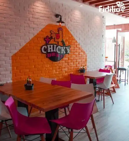 رستوران چیکی بیف: فضایی شیک و دلپذیر با دکوراسیون دیوارهای آجری سفید و نارنجی، میزهای چوبی و صندلی‌های مدرن صورتی.