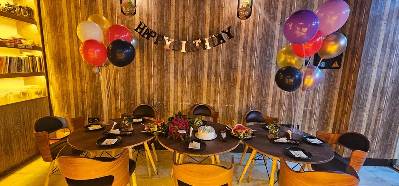 کافه لوف: دکوراسیون جشن تولد در فضایی گرم و چوبی با میزهای آماده، کیک، بادکنک و گل، مناسب ساخت لحظات شیرین و به یادماندنی.