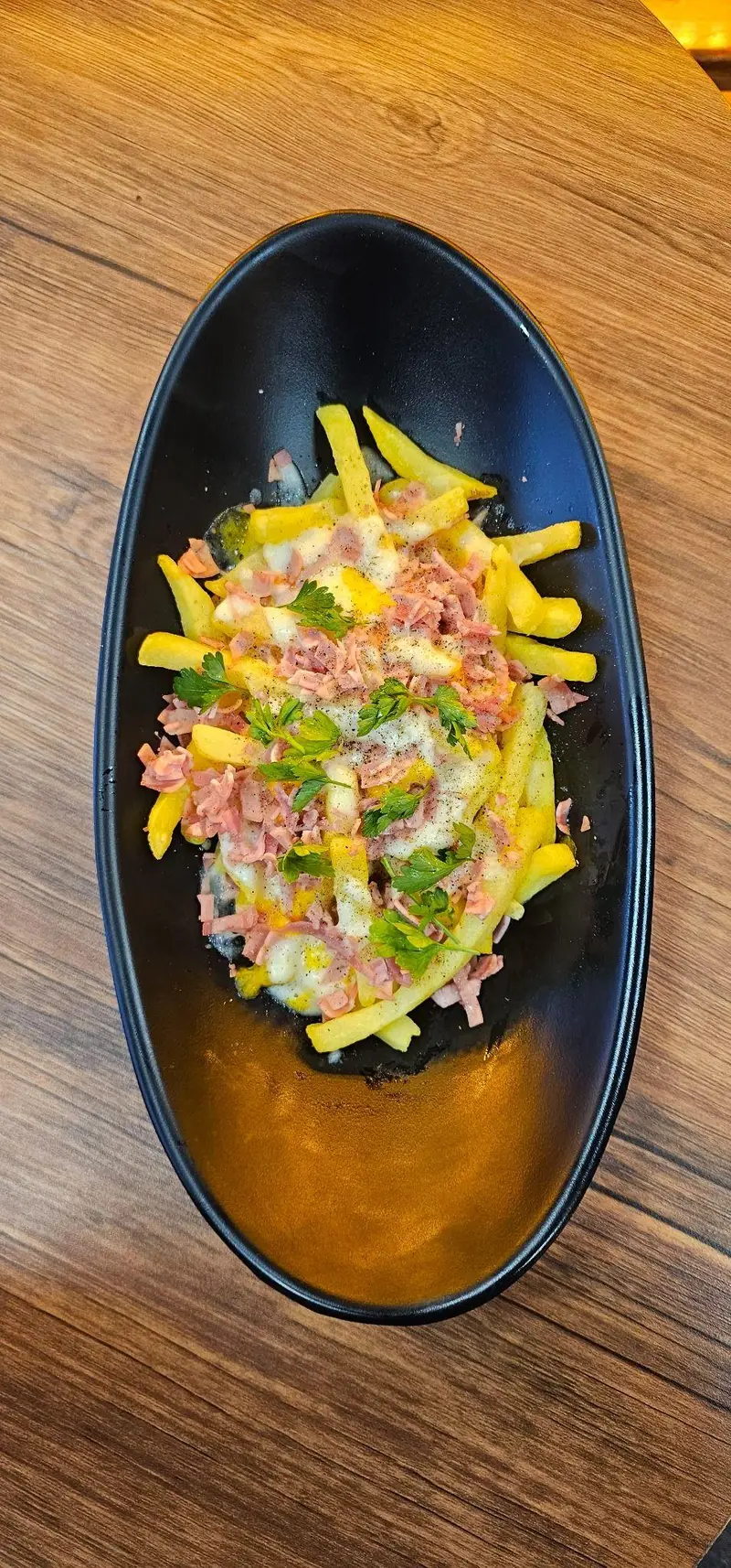 سیب زمینی سرخ کرده با پنیر آب شده، تکه‌های ژامبون و جعفری تازه در ظرف مشکی، تجربه‌ای دلنشین از کافه لوف.