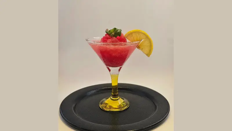 کوکتل اسلاش میوه‌ای قرمز کافه لوف با تزیین لیمو و نعناع، نوشیدنی خنک و دلچسب تابستانی در لیوان مارتینی روی صفحه مشکی.