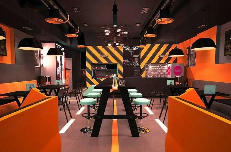 طراحی داخلی جذاب و مدرن فست فود RAMCY با تم جاده و صنعتی، رنگ‌های زنده نارنجی، مشکی و زرد، نورپردازی خاص و مبلمان شیک برای مشتریان.
