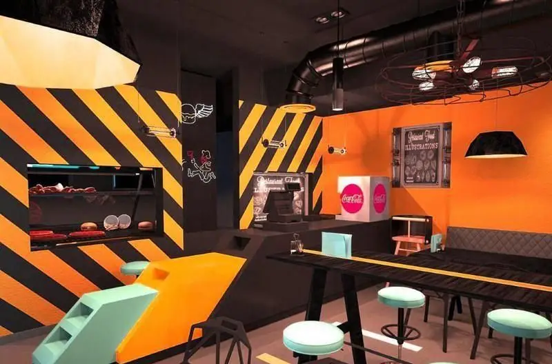 طراحی داخلی خاص و رنگارنگ رستوران فست فود RAMCY با تم صنعتی، دیوارهای نواری هشداردهنده و میزهای شیک برای تجربه غذایی دلنشین.