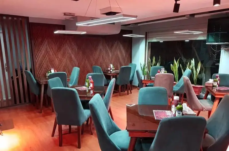محیط داخلی شیک و مدرن فست فود ویست فود، با میز و صندلی‌های فیروزه‌ای، دکوراسیون چوبی و نورپردازی دلپذیر.