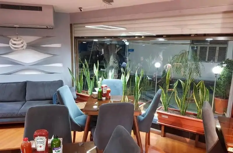 نمایی از فضای داخلی رستوران فست فود ویست فود با چیدمان مدرن، میز و صندلی‌های شیک، مبل راحتی و گیاهان سبز کنار پنجره بزرگ.