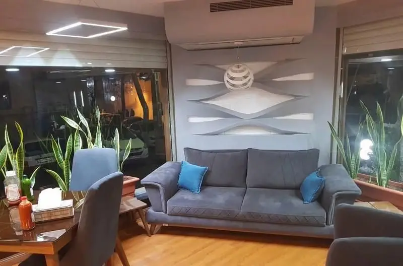 فضای داخلی شیک فست فود ویست فود با دکوراسیون مدرن، مبل راحتی خاکستری، میز غذاخوری چوبی، گلدان‌های گیاه مار و پنجره‌های بزرگ رو به خیابان.