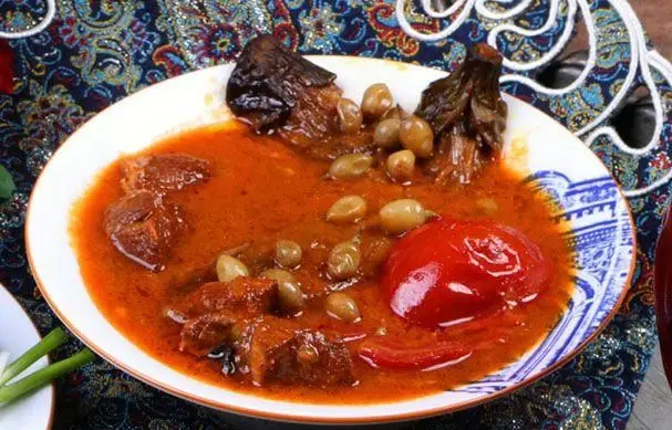 یک بشقاب خورش سنتی و لذیذ ایرانی شامل گوشت، بادمجان، گوجه و غوره، آماده سرو در کافه رستوران وکیل التجار.