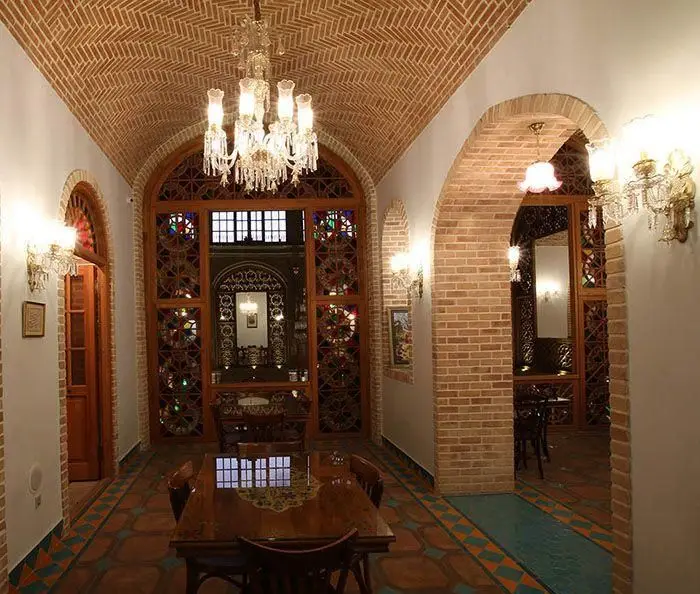 کافه رستوران وکیل التجار؛ طراحی داخلی سنتی با سقف آجری و قوس‌های زیبا، پنجره‌های ارسی رنگارنگ، لوستر چشم‌نواز و فضایی دلنشین و اصیل.