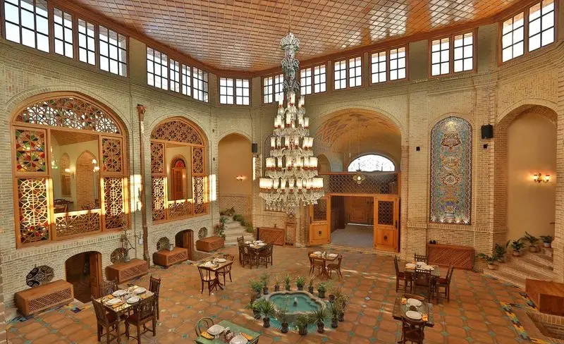 فضای دلنشین کافه رستوران وکیل التجار کرمان با معماری اصیل ایرانی، حوض زیبا، پنجره‌های ارسی و سقف چوبی مزین.