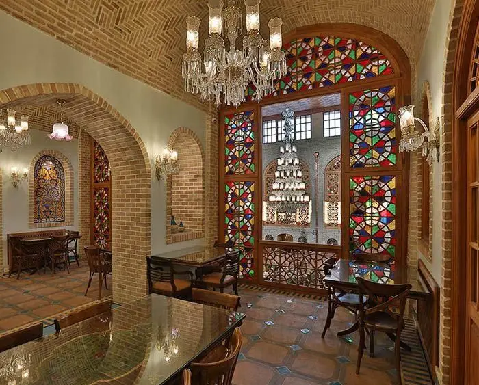 فضای داخلی کافه رستوران وکیل التجار با معماری سنتی ایرانی، آجرکاری زیبا، پنجره‌های ارسی رنگارنگ و لوسترهای مجلل.