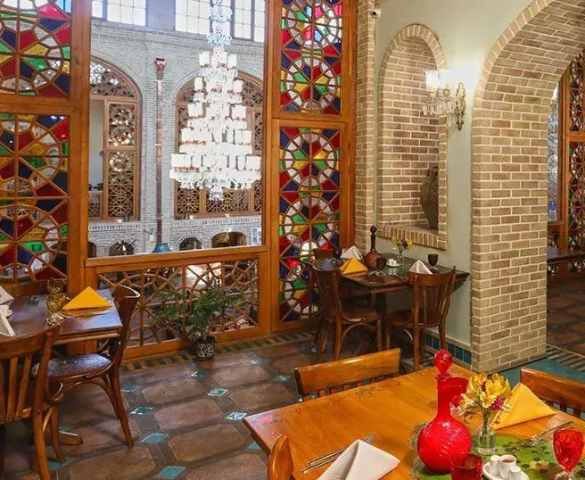 فضای داخلی کافه رستوران وکیل التجار اصفهان با معماری سنتی ایرانی، پنجره‌های ارسی رنگارنگ، لوستر بزرگ و دکوراسیون دلنشین.