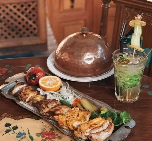 سفره‌ای از جوجه کباب ایرانی، گوجه کبابی، ترشیجات و نوشیدنی تازه در کافه رستوران سنتی وکیل التجار اصفهان