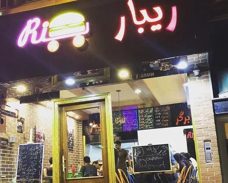 نمای بیرونی جذاب فست فود برگر ریبار برگر در شب با تابلوی نئون. منوی متنوعی از برگر و ساندویچ‌های تازه و خوشمزه.