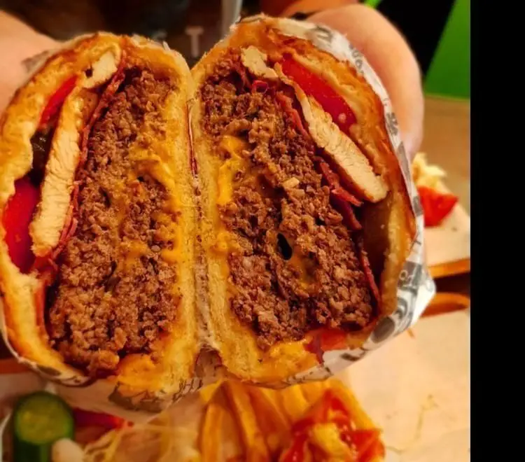 برگر ویژه ریبار برگر: ساندویچ پرمغز فست فود با گوشت فراوان، پنیر ذوب شده، مرغ و بیکن، از وسط برش خورده و آماده سرو.