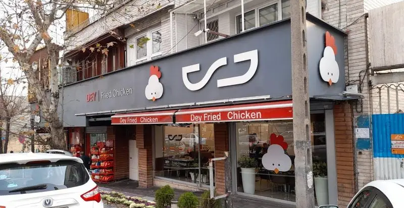 تصویری روشن از نمای بیرونی شعبه مرغ سوخاری دی (Dey Fried Chicken) در خیابان با تابلوی مدرن و لوگوی جوجه.