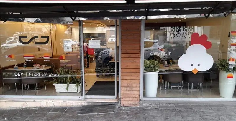 نمای بیرونی رستوران مرغ سوخاری دی (DEY Fried Chicken) با لوگوی سر مرغ و ویترین شیشه‌ای. ارائه دهنده منوی کامل از ساندویچ، برگر و پیتزا.