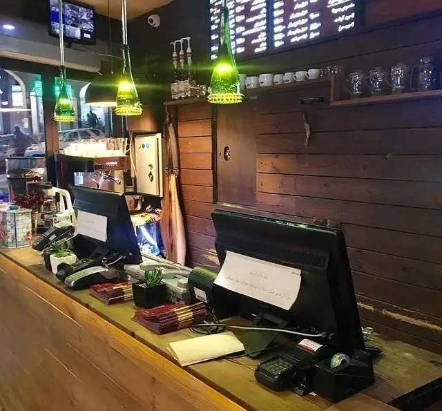 نمای داخلی فست فود رسپینا، شامل پیشخوان مجهز به دو صندوق فروش، مانیتورهای POS، دستگاه پوز، نورپردازی خلاقانه با بطری‌های سبز و منوی قیمت‌ها.