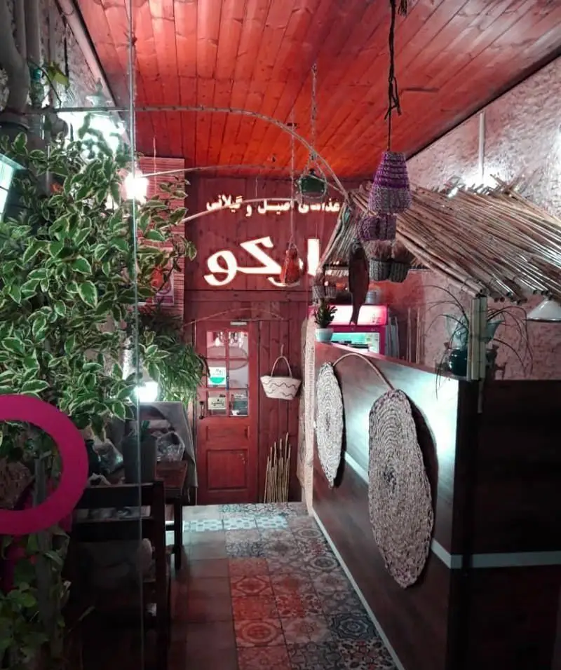 فضای داخلی دنج و سنتی رستوران گیلانی بارکو با سقف چوبی قرمز، گیاهان سرسبز و کفپوش طرح‌دار. مناسب برای لذت بردن از غذای اصیل گیلانی.