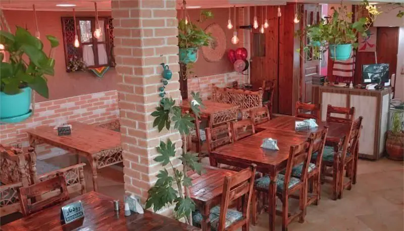 فضای داخلی دلنشین و سنتی رستوران گیلانی بارکو با میز و صندلی‌های چوبی خاص، دیوارهای آجری و گیاهان آویز.