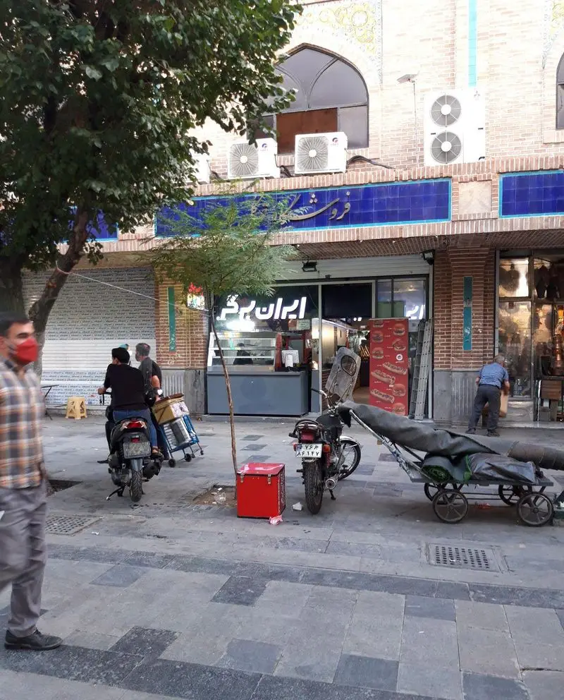 نمایی از رستوران فست فود ایران برگر (سرزمین سوخاری) در خیابانی شلوغ با موتورسیکلت‌های آماده دلیوری غذا.