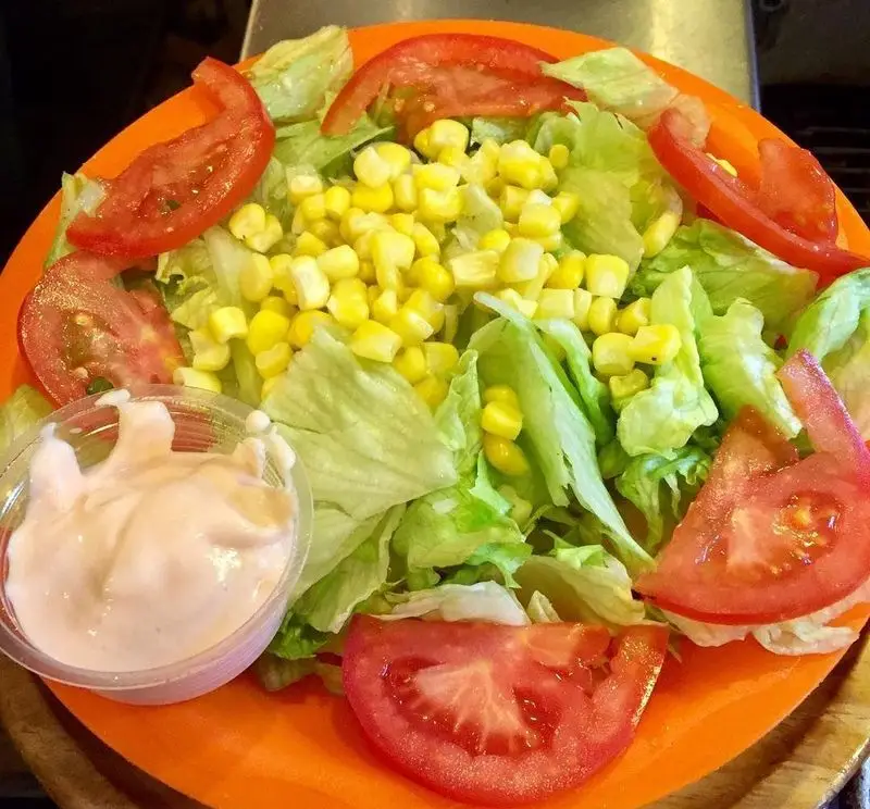 سالاد خوشمزه فست فود هیزم با کاهو تازه، ذرت شیرین، گوجه‌های برش خورده و سس مخصوص خانگی در بشقاب نارنجی.