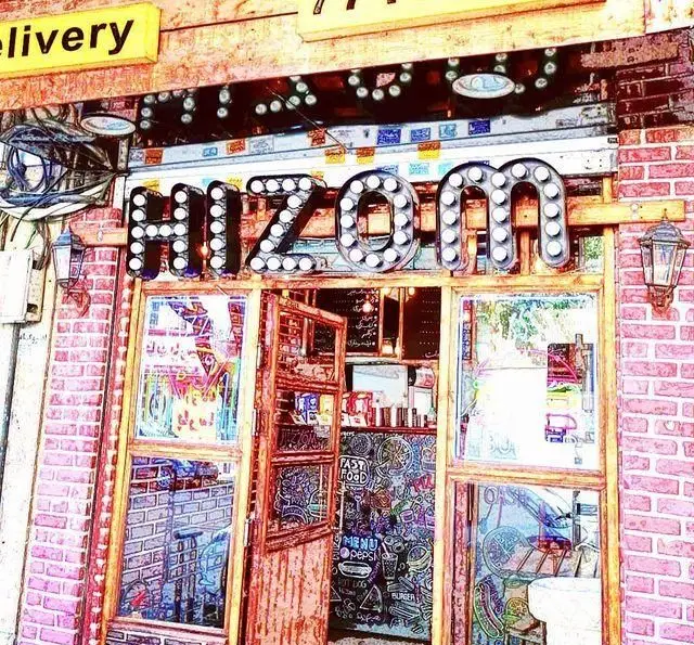 ورودی جذاب فست فود هیزم با تابلوی چراغ دار HIZOM، دیوارهای آجری، درب چوبی و شیشه ای. مناسب سفارش آنلاین و دلیوری غذا.