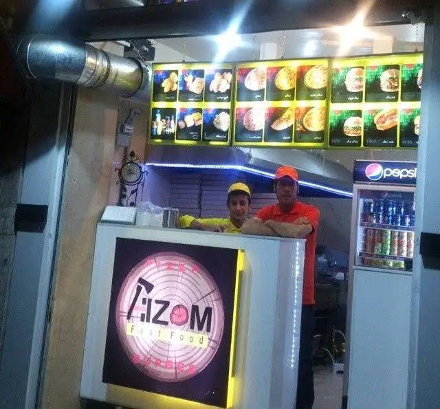 فست فود هیزم: دو کارمند خوش برخورد در پشت پیشخوان، همراه با منوی کامل پیتزا، ساندویچ، برگر و مرغ سوخاری برای مشتریان