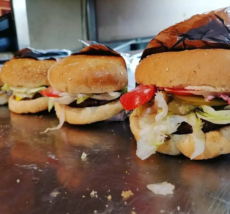 سه برگر لذیذ فست فود هیزم با ترکیبات تازه شامل نان کنجدی، گوشت، کاهو، گوجه، پیاز، خیارشور و سس مخصوص، آماده ارائه در رستوران.