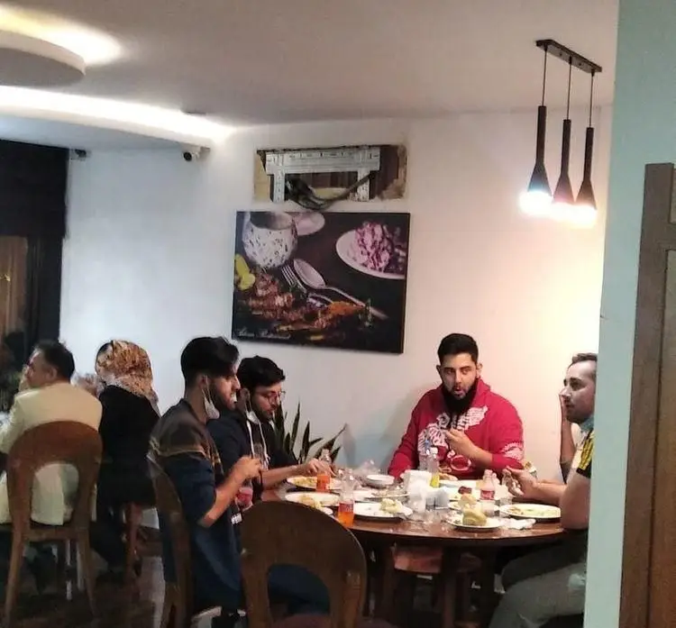 مشتریان در حال لذت بردن از غذا در رستوران آدانا، یک میز گرد با انواع خوراکی‌ها و نوشیدنی‌ها در فضایی دلنشین.