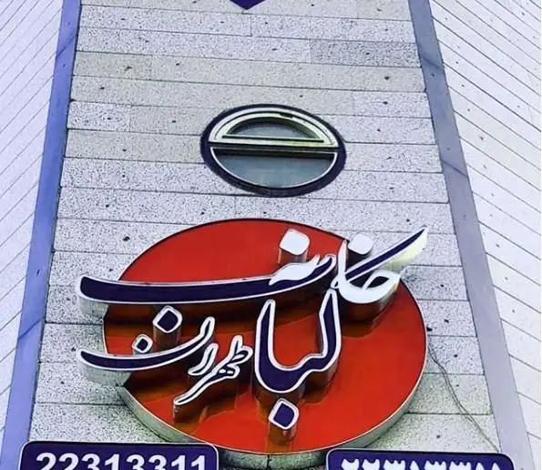 تابلوی بزرگ و مدرن "خانه کباب طهران" با رنگ قرمز و حروف برجسته بر روی ساختمان سنگی، نمایانگر رستوران کباب محبوب تهران.