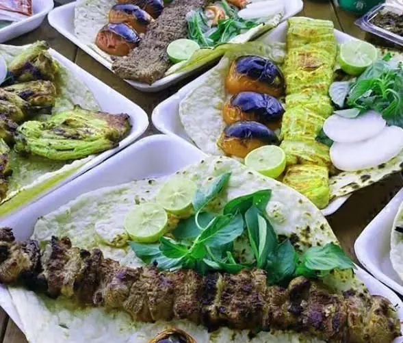 میز مملو از انواع کباب ایرانی شامل کوبیده و جوجه به همراه نان تازه، گوجه کبابی، لیمو و سبزیجات معطر از خانه کباب طهران.