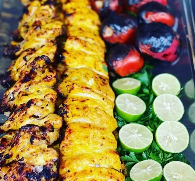 دو سیخ جوجه کباب طلایی و آبدار، همراه با گوجه کبابی و برش‌های لیمو تازه. غذای اصیل ایرانی در رستوران حمید.