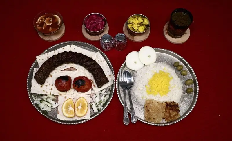 سفره غذای سنتی ایرانی مطبخ فر و دیگ شامل کباب کوبیده، پلو زعفرانی، مخلفات متنوع نظیر ترشی، زیتون، سوپ و ته دیگ. غذای کامل و لذیذ.