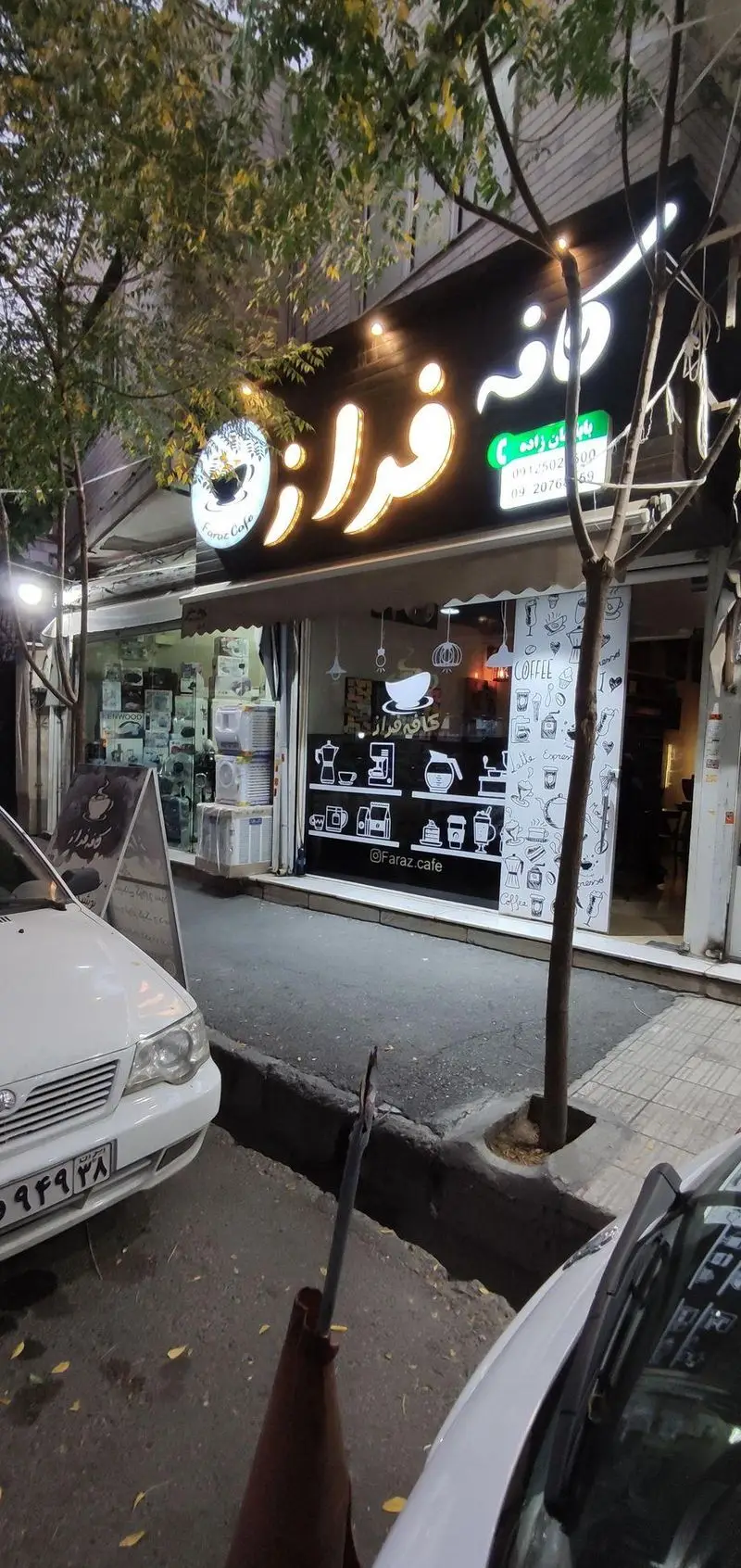 نمای بیرونی و جذاب کافه فراز در شب با تابلوی روشن و لوگوی Faraz Cafe. ویترین با طرح‌های متنوع قهوه و آدرس اینستاگرام.